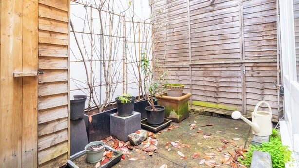 A wooden shed with potted plants and a watering can on the ground. - Cosy 1BD Hideaway in Paddington (London)