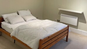 A bedroom with a wooden bed, white bedding, a ceiling light fixture, and a wall-mounted heater. - Cosy 1BD Hideaway in Paddington (London)