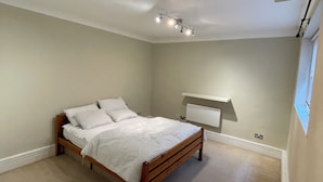 A bedroom with a wooden bed, white bedding, a ceiling light fixture, and a white air conditioning unit. - Cosy 1BD Hideaway in Paddington (London)