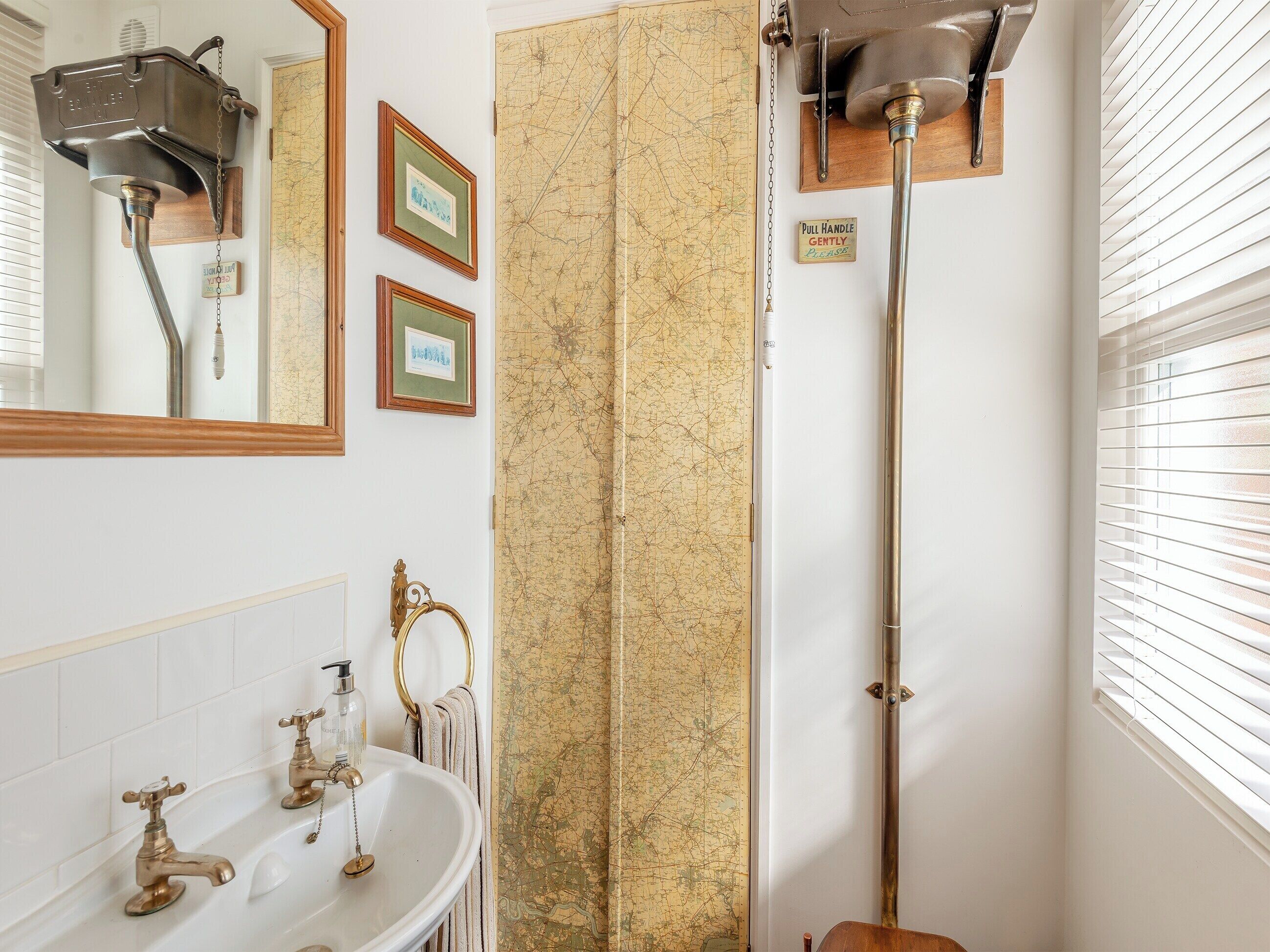 A bathroom with a sink, two framed pictures, a map, and a pull handle sign.