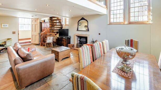 A spacious living room with a high ceiling, a fireplace, a dining table with chairs, and a staircase leading to an upper level. - Sympathetically stunning restored property. (Rickling Green, near Saffron Walden)