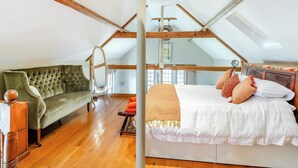 A loft bedroom with a bed, a green sofa, wooden beams, and a skylight. - Sympathetically stunning restored property. (Rickling Green, near Saffron Walden)