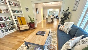Una sala de estar con un sofá azul, una mesa de centro de madera con un libro, un tapete estampado y una estantería llena de libros.