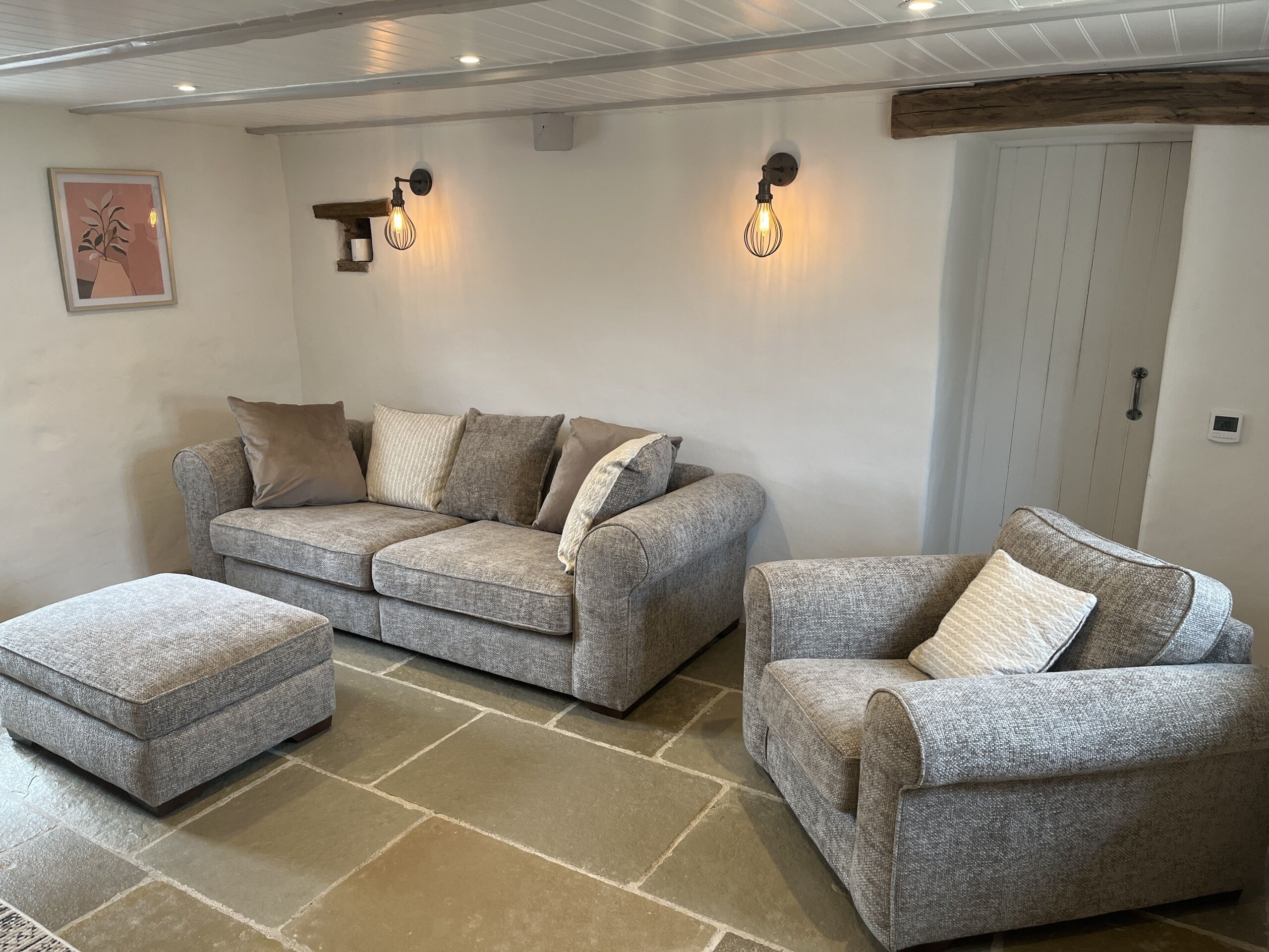 A cozy living room with a grey sofa set, a matching ottoman, and two wall-mounted light fixtures.