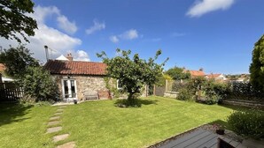 A backyard with a wooden deck, a stone building, and a well-maintained lawn. - Blacksmiths Cottages (Filey)