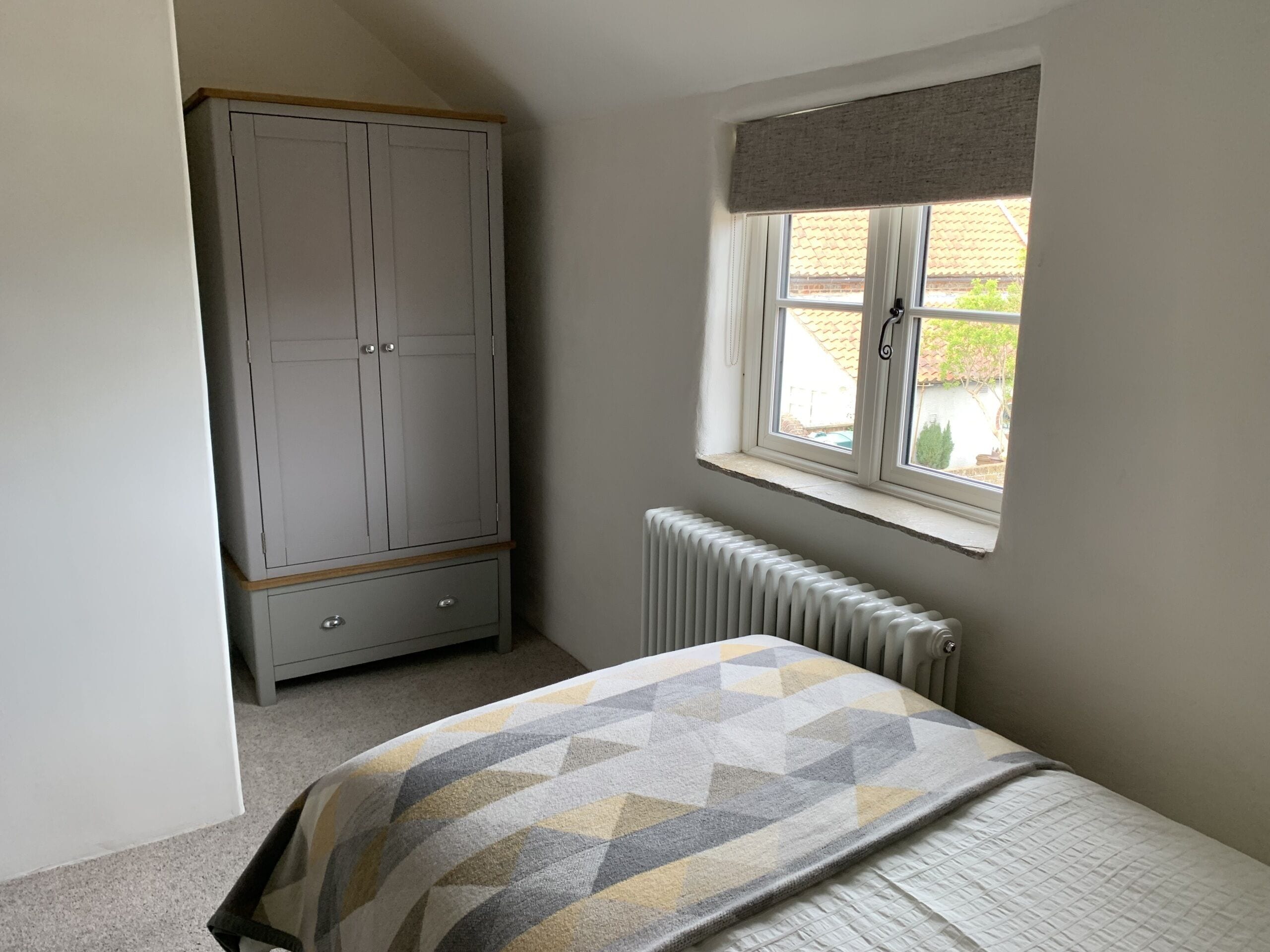 A bedroom with a bed, a wardrobe, a window with a view, and a radiator.