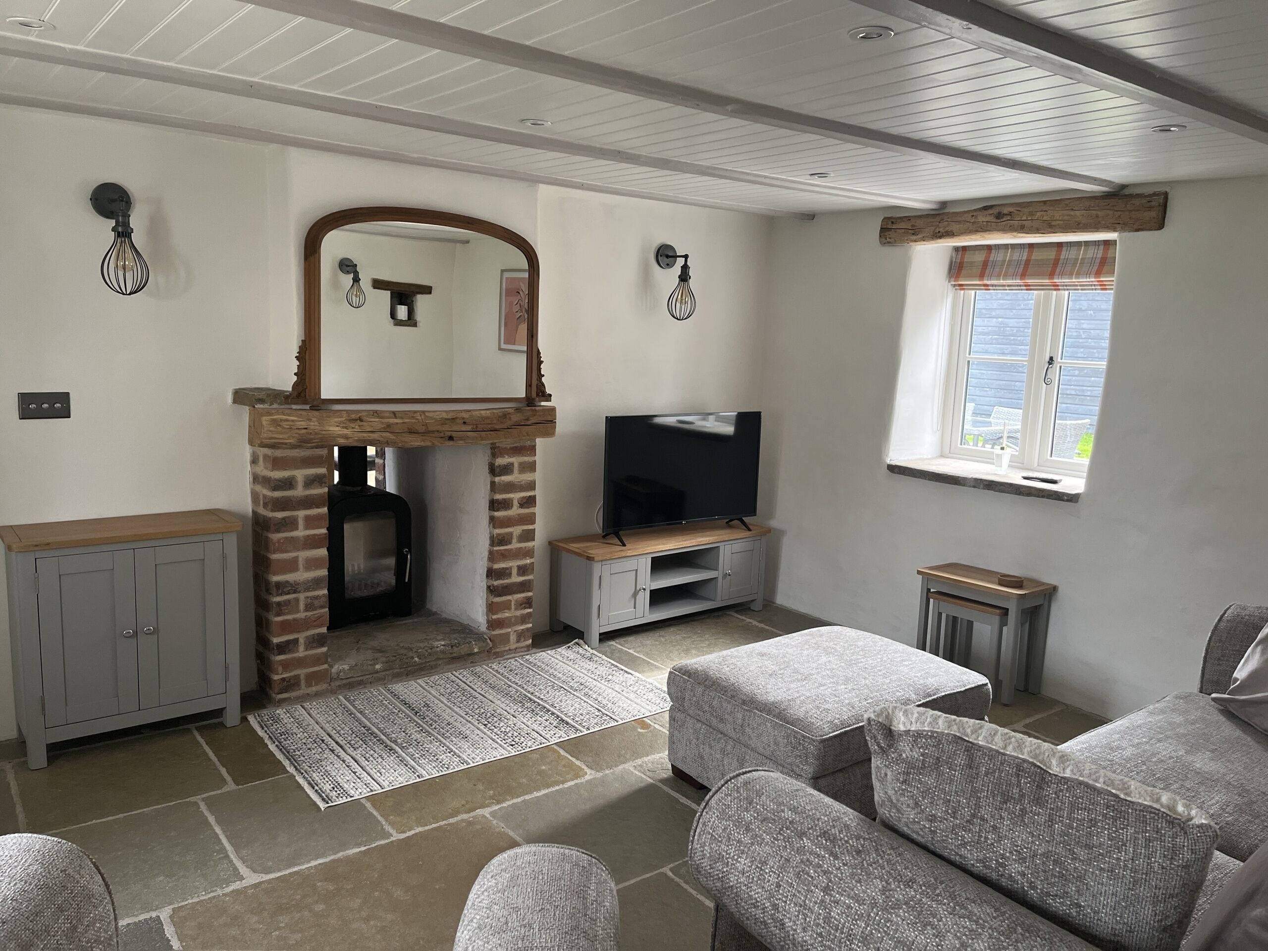 A living room with a fireplace, television, grey sofas, and a window with curtains.