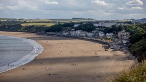 A coastal town with a sandy beach, a promenade lined with buildings, and a backdrop of hills. - Blacksmiths Cottages (Filey)