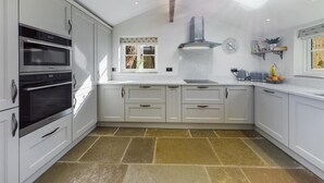 A modern kitchen with white cabinetry, a built-in oven, and a stone tile floor. - Blacksmiths Cottages (Filey)