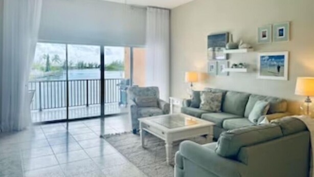 Ein geräumiges Wohnzimmer mit großem Fenster, Deckenventilator, Sofa, Couchtisch und Balkon mit Geländer.