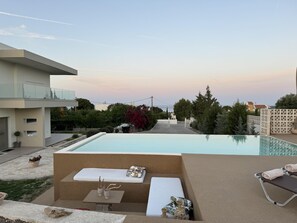 Ein moderner Poolbereich im Freien mit Liegestuhl und kleinem Tisch, umgeben von einem angelegten Garten und Blick auf die Nachbarschaft.