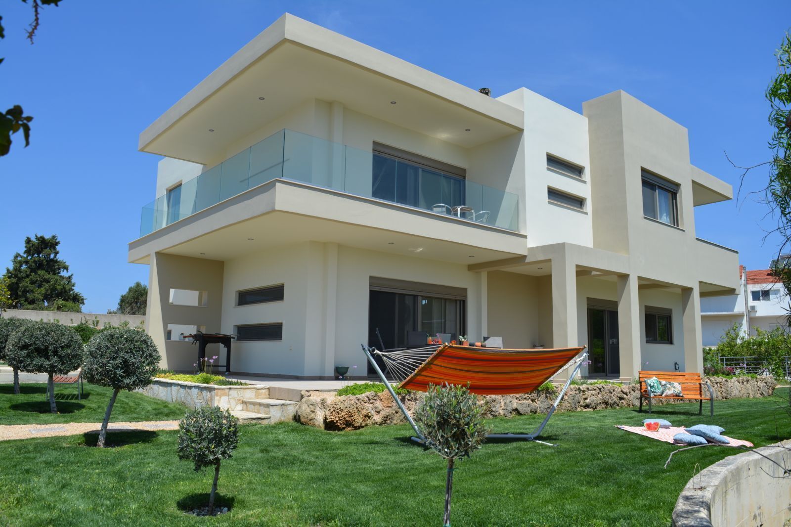 A modern two-story house with a balcony, a hammock, and a well-maintained lawn.