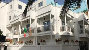 A multi-story building with balconies, a flag, and potted plants.