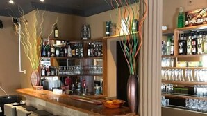 A bar area with a long counter, multiple stools, and shelves stocked with bottles and glasses.