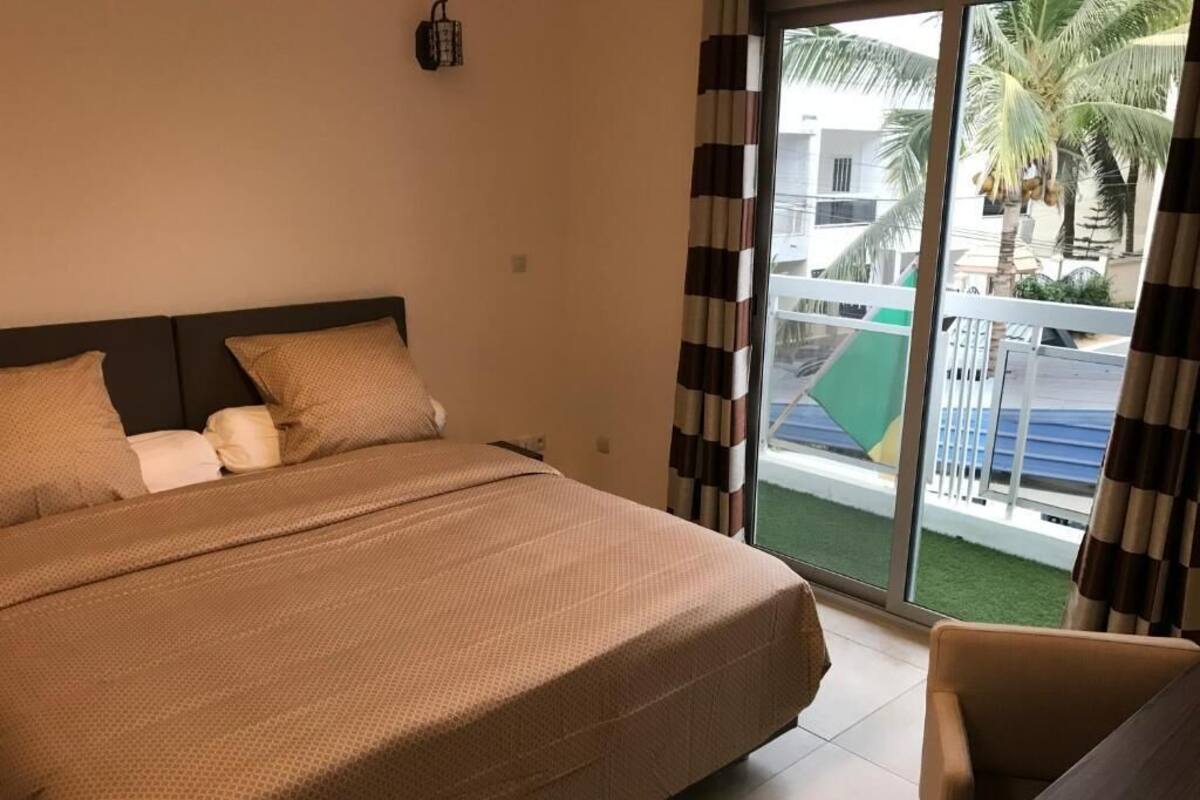 Une chambre d’hôtel avec un lit, une chaise et une vue sur un balcon bordé de palmiers.