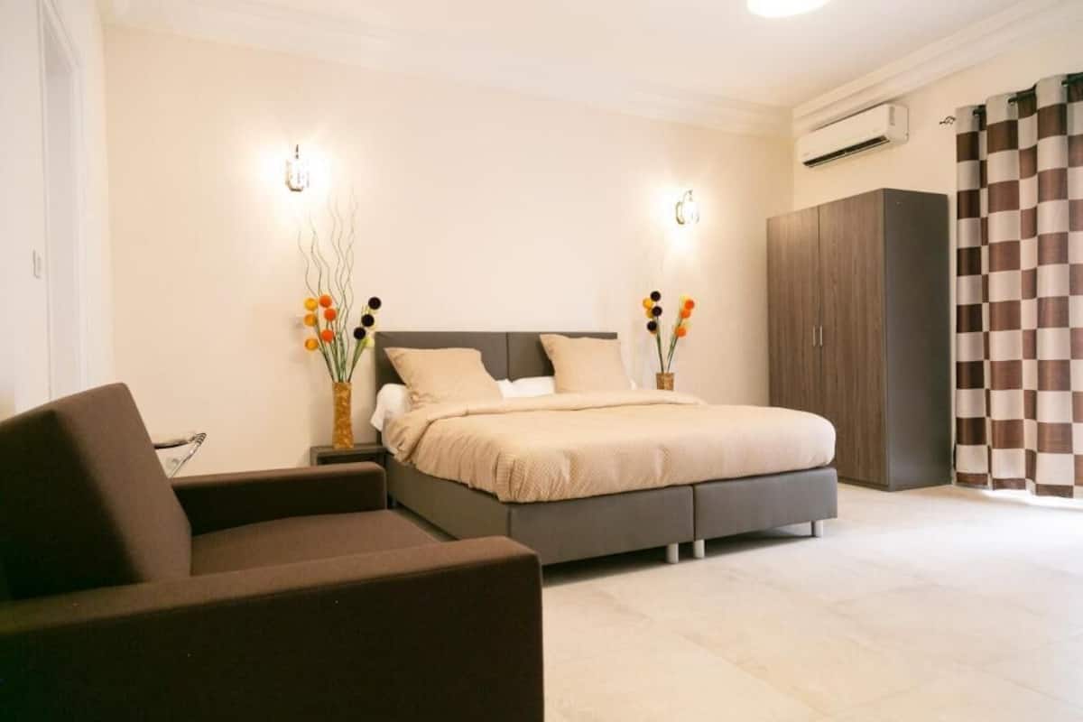 Une chambre à coucher comprenant un lit, des tables de chevet, un canapé, une armoire et des vases décoratifs.