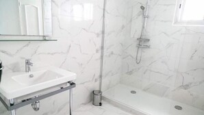 A bathroom with a white marble sink, a glass shower enclosure, and a metal trash can.