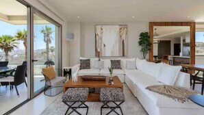 Een moderne woonkamer met een witte bank, een bijzettafeltje en een groot raam met uitzicht op palmbomen.