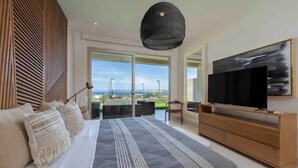 Een moderne slaapkamer met een groot bed, een televisie op een houten standaard en een balkon met uitzicht.