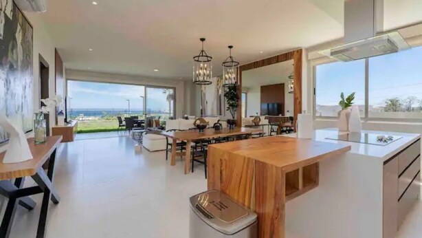 Een ruime keuken met een centraal eiland, grote ramen en uitzicht op de omgeving.