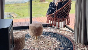 Une pièce dotée d’une grande fenêtre, d’un fauteuil suspendu, d’un petit pouf et d’un tapis à motifs.