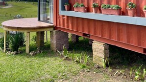 Une structure extérieure moderne, dotée d’une paroi vitrée, d’une table en bois et de plantes en pot.