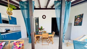 A cozy dining area with a wooden table and chairs, a kitchen with blue cabinets, and a decorative plant hanging from the ceiling. - Zandoli, swimming pool, sea view, peaceful, garden (Sainte-Luce)
