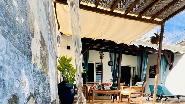 A pool with a waterfall feature, a covered seating area with a table and chairs, and a potted plant. - Zandoli, swimming pool, sea view, peaceful, garden (Sainte-Luce)