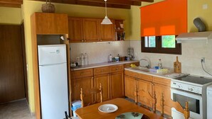 A compact kitchen with wooden cabinets, a white refrigerator, a stove, and a dining table with chairs.