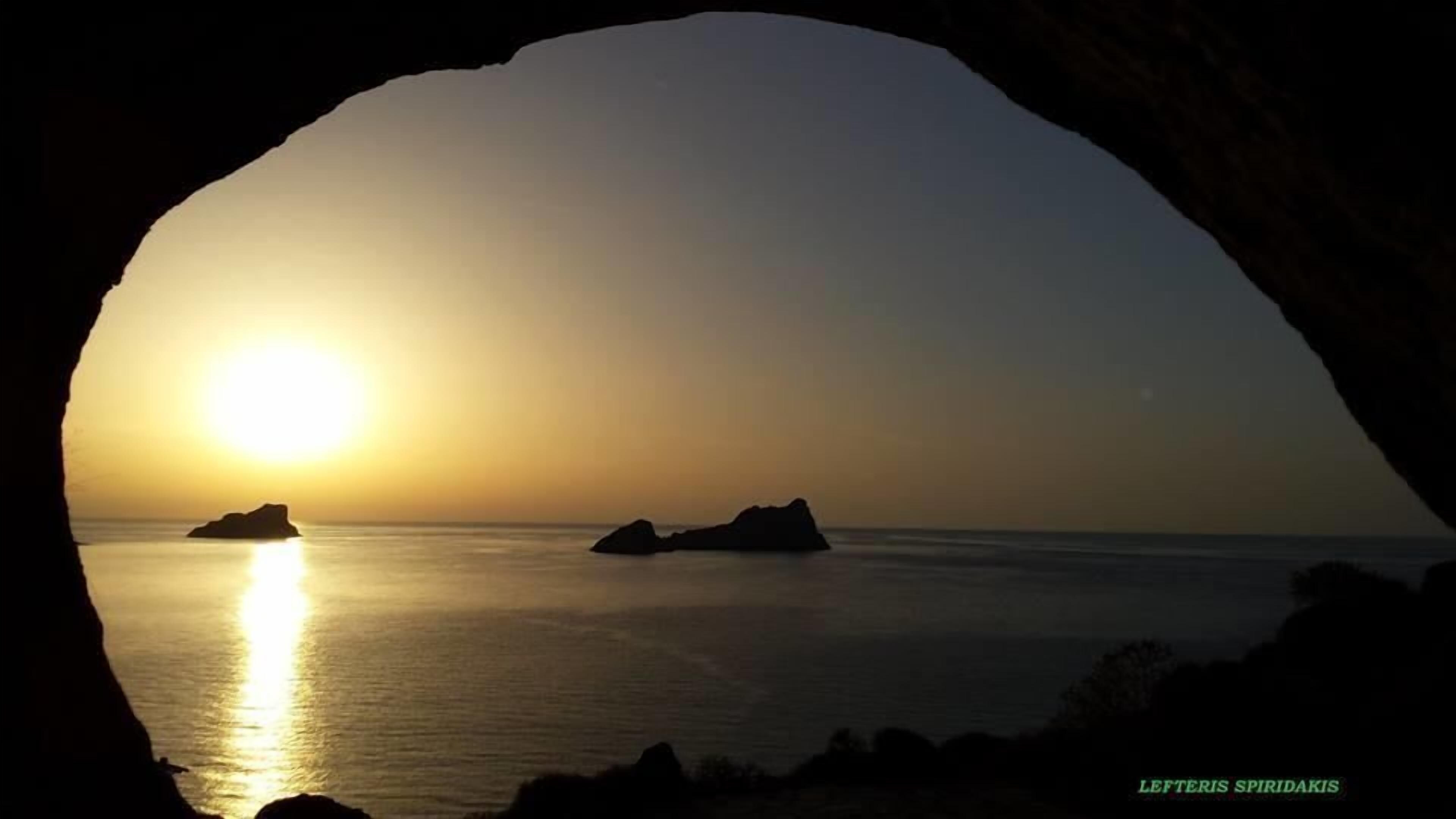 A sunset view through an archway with calm sea and distant islands.