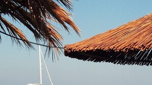 A beach scene with a sailboat, a person standing by the water, and a table with a plant.