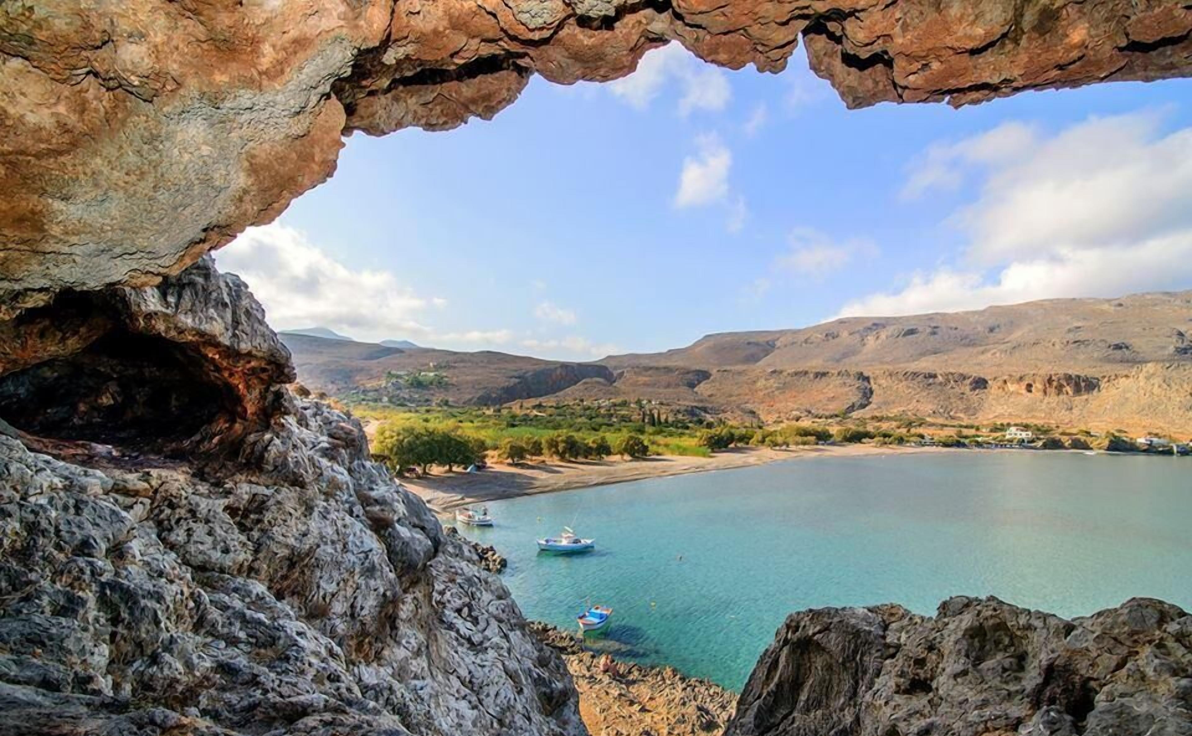 A natural rock formation with a view of a lake, boats, and distant hills.