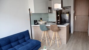 Eine moderne Küche mit Kochinsel, zwei Barhocker, einem blauen Sofa und einem kleinen, runden Tisch mit Dekoration.