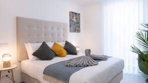 A neatly made bed with a tufted headboard, a bedside table with a lamp, and a large window with sheer curtains. - Contemporary modern apartment [119] (Lagos)