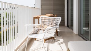 Un balcón con mobiliario de mimbre blanco, una mesa de madera y vista al exterior del edificio.