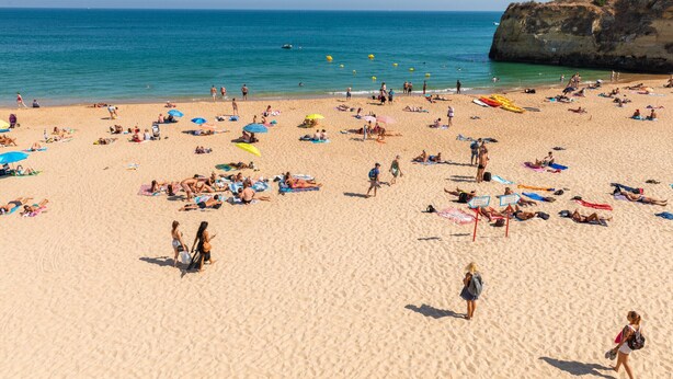 Una playa concurrida donde gente toma el sol y nada, con un acantilado rocoso al fondo.