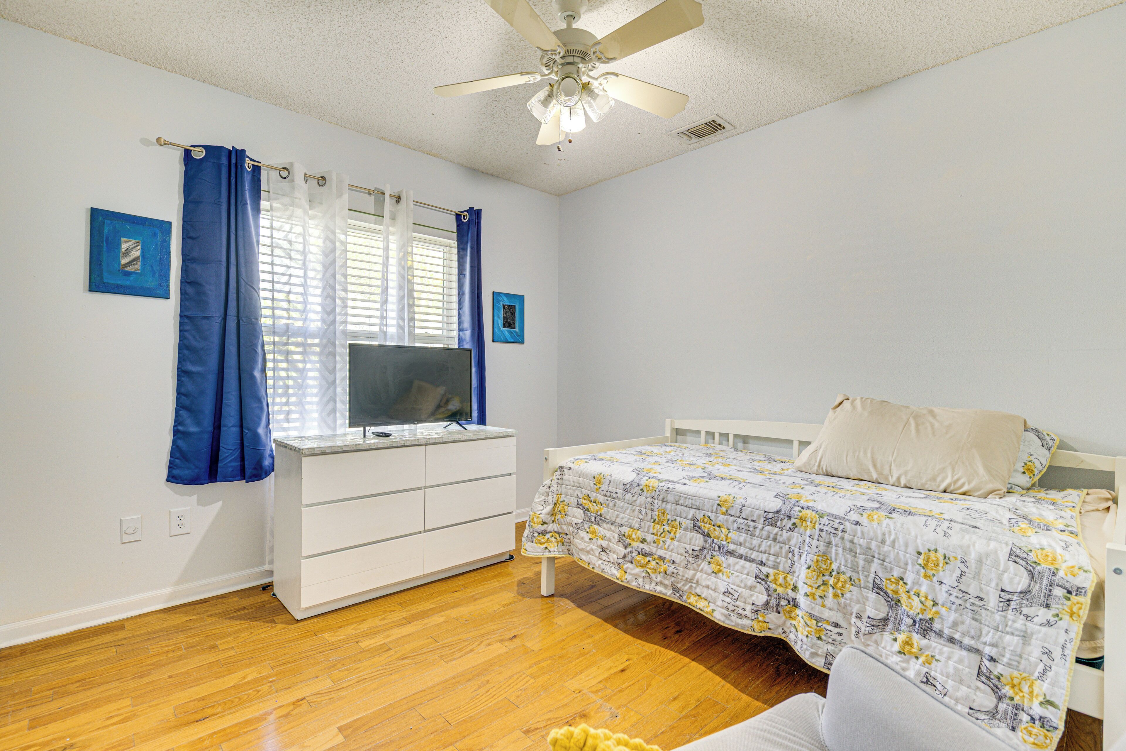 A bedroom with a bed, a TV, a desk, and a ceiling fan.
