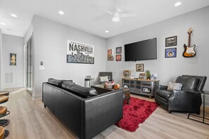 A modern living room with a black leather sofa, a red rug, and a flat-screen TV mounted on the wall.