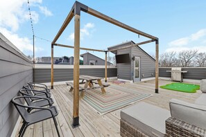 A rooftop deck with a wooden pergola, outdoor seating, and a barbecue area.