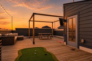 A rooftop deck with a wooden pergola, seating, a table, and a mini-golf setup.