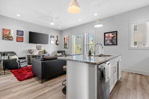 A modern living space with a kitchen island, a flat-screen TV, and artwork on the walls.