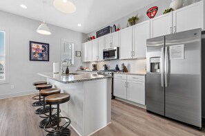 A modern kitchen with white cabinets, a stainless steel refrigerator, a microwave, and a bar area with stools.