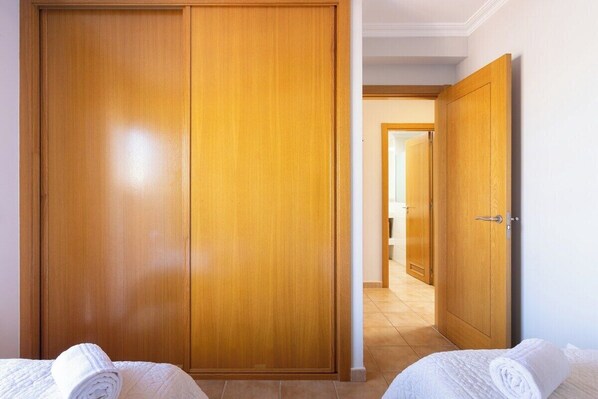 A hotel room with a wooden wardrobe, a bed with a white duvet, and a bathroom visible through an open door.