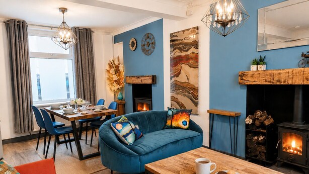 Een gezellige woonkamer met een blauwe bank, een eettafel en een open haard.