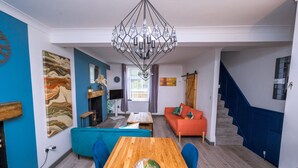 Een moderne woonkamer met een houten eettafel, blauwe stoelen, een rode bank en een trap.