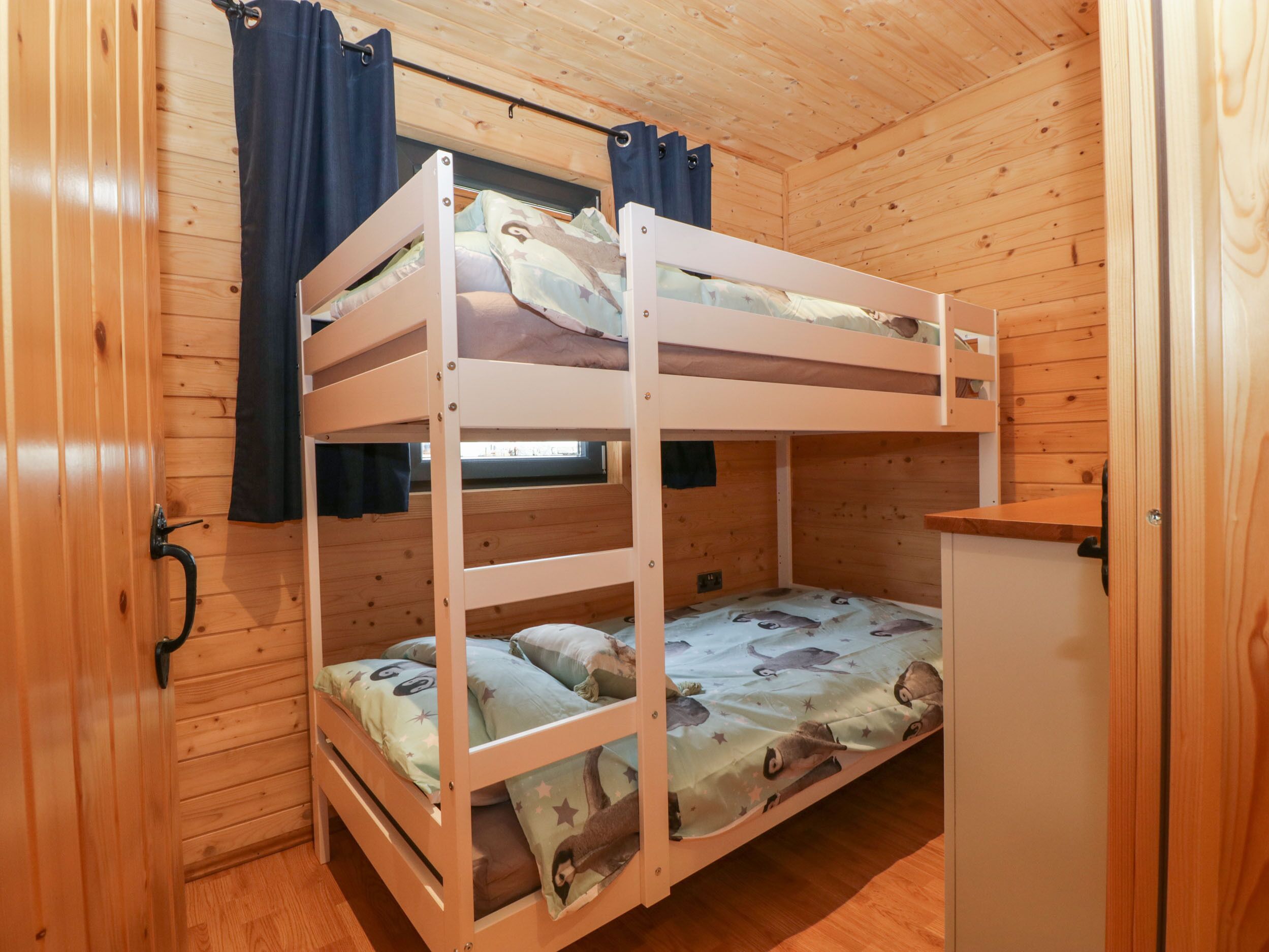 A bunk bed room with a window, wooden walls, and a small white cabinet.