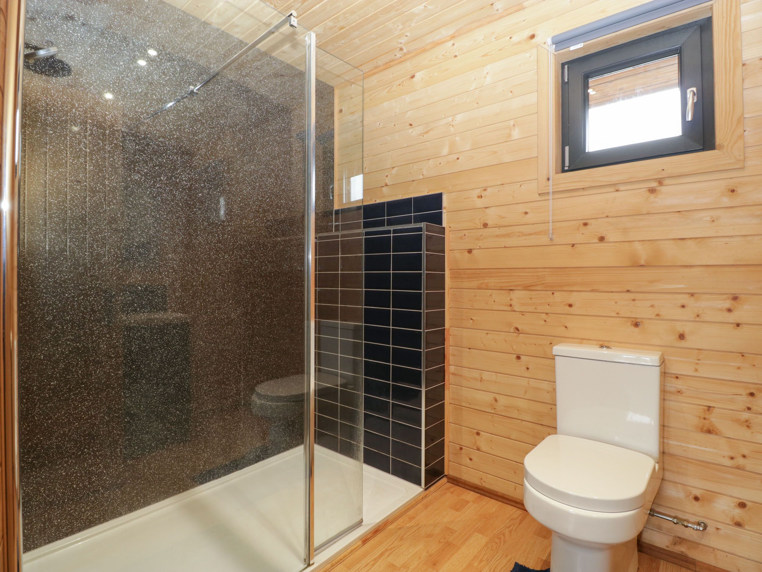 Un baño con cabina de ducha de vidrio, inodoro y una ventana pequeña.