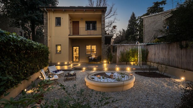 Ein zweistöckiges Haus mit einer Terrassenfläche, die Sitzgelegenheiten und einen Rundgarten bietet.