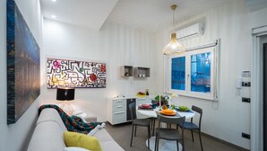 Ein modernes Wohnzimmer mit einer Couch, einem Esstisch mit Stühlen, einer Pendelleuchte und einem großen abstrakten Gemälde an der Wand.