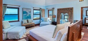 A bedroom with a large bed, two seating areas, a wooden headboard, and a view of the ocean.